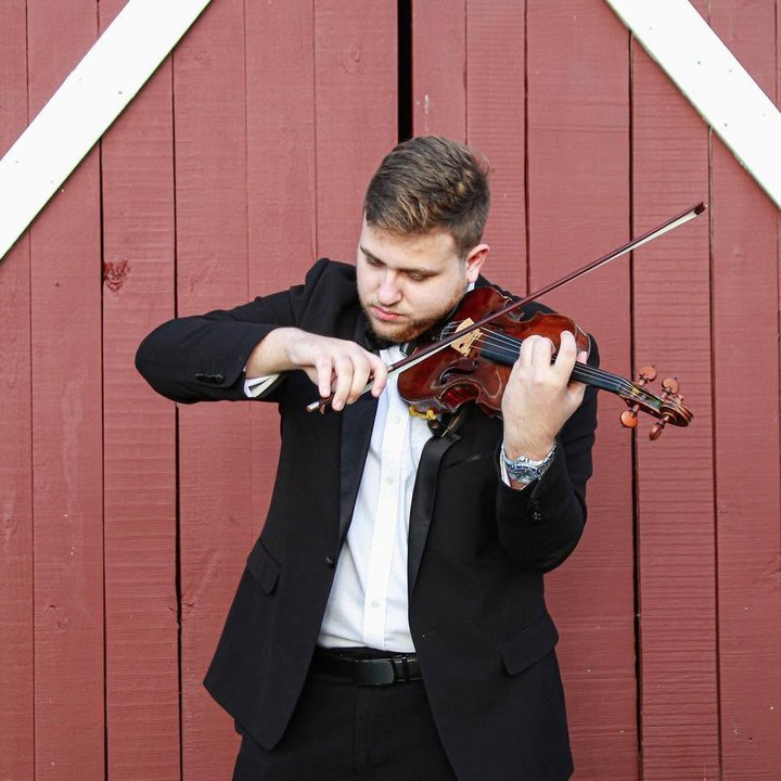 George Pekarsky in concert black, playing violin against a red barn door